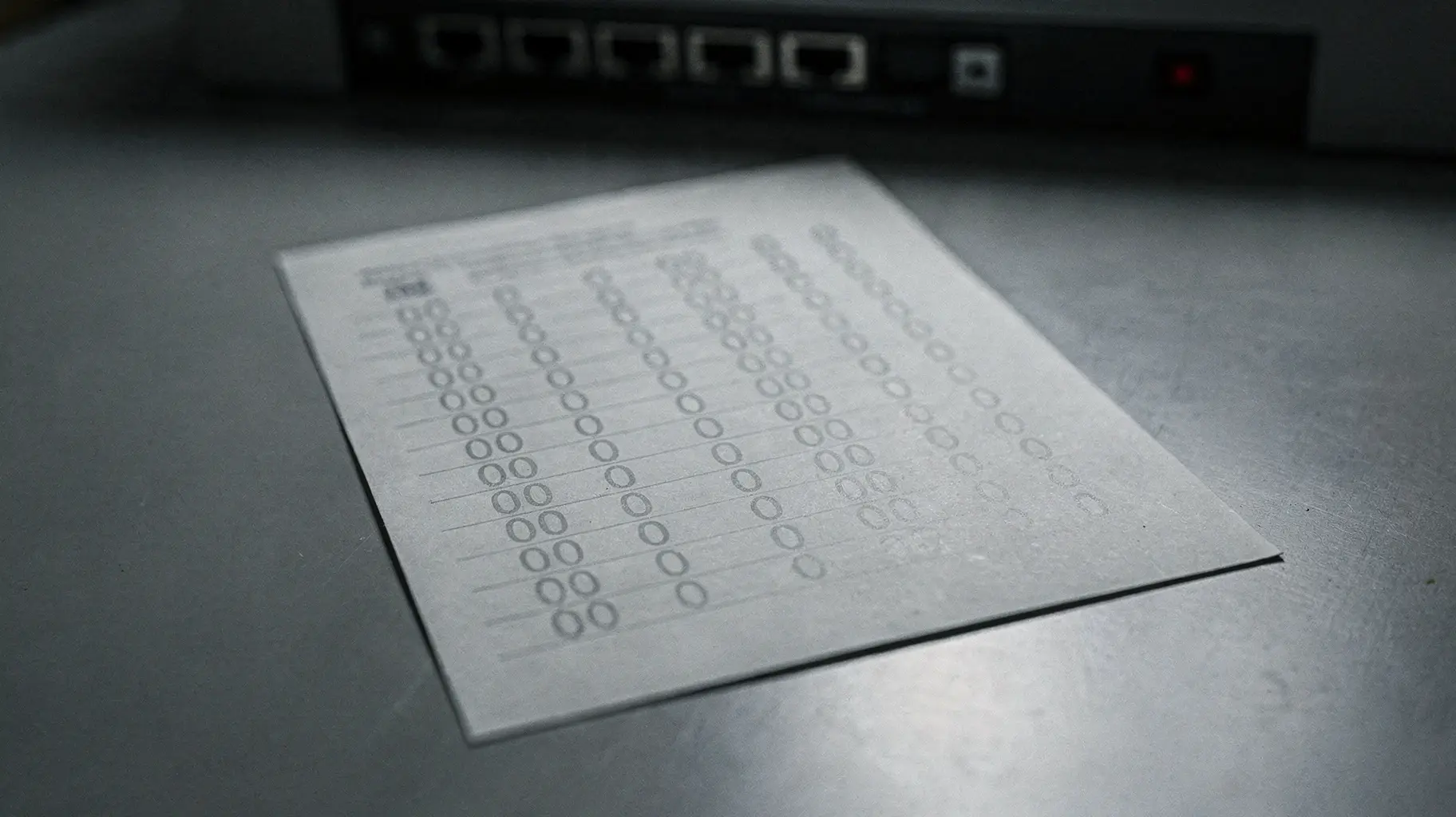 An illustration of a printed registry extract with a column of zeros on a grey desk, with an out-of-focus switch port panel behind it.